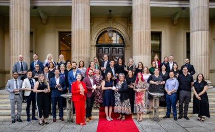 A group of UQ researchers holding award trophies standing out the front of a sandstone building on a red carpet